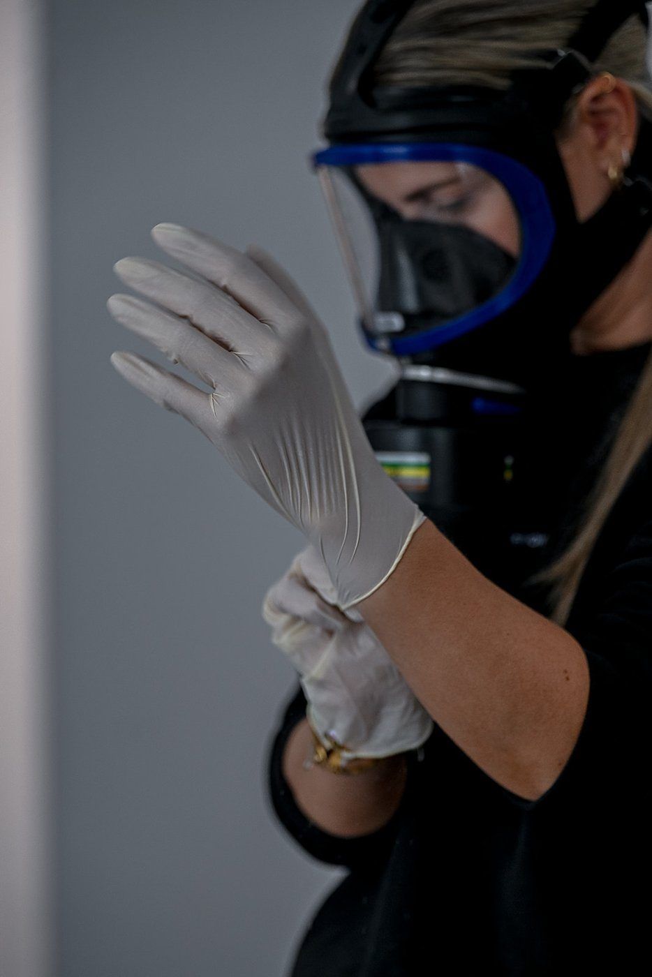 Frau mit Atemschutzmaske zieht einen Schutzhandschuh an