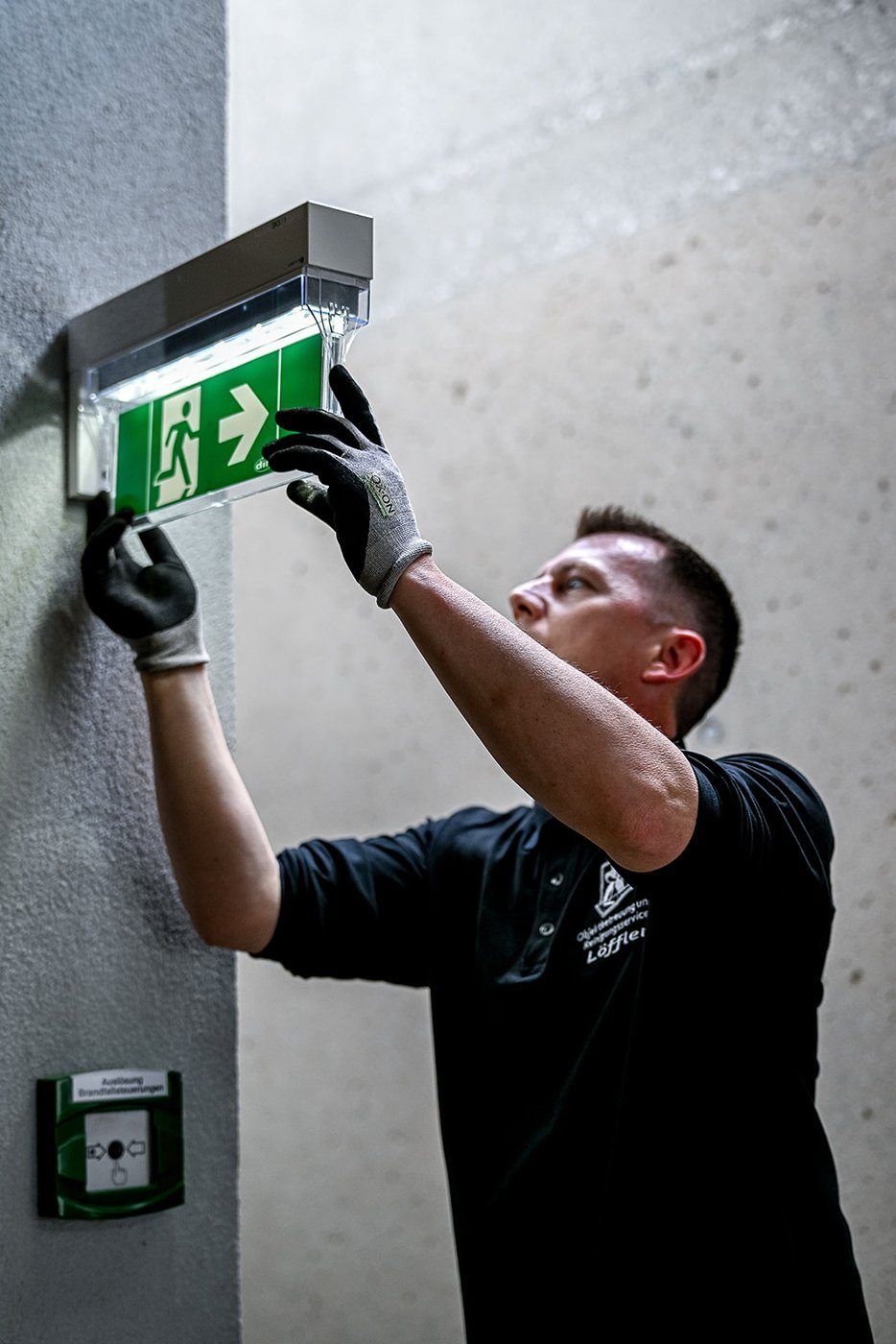 Mann mit Schutzhandschuhen montiert ein Notausgang-Schild an der Wand