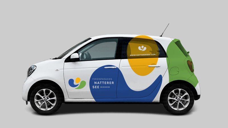 Visualisierung: Kleinwagen mit der Beschriftung „Ferienparadies Natterer See“ in Blau, Gelb und Grün