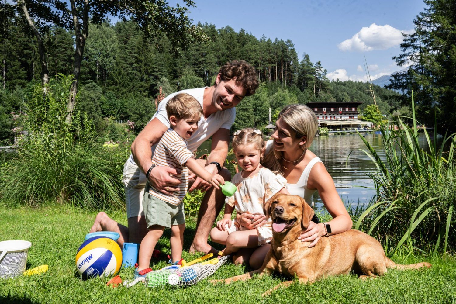 Familie mit zwei Kindern und einem Hund spielt auf einer Wiese am Natterer See