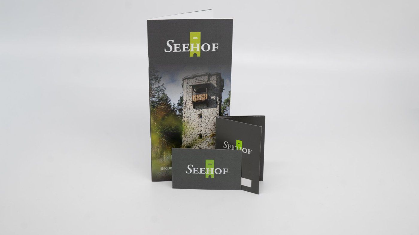 Folder und Karten des Seehofs mit grünem Logo, auf dem Folder ein Holzturm im Wald
