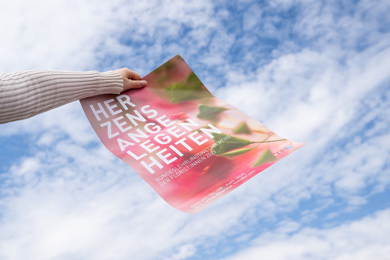 Hand hält ein Plakat „Herzensangelegenheiten“ vor blauem Himmel mit Wolken