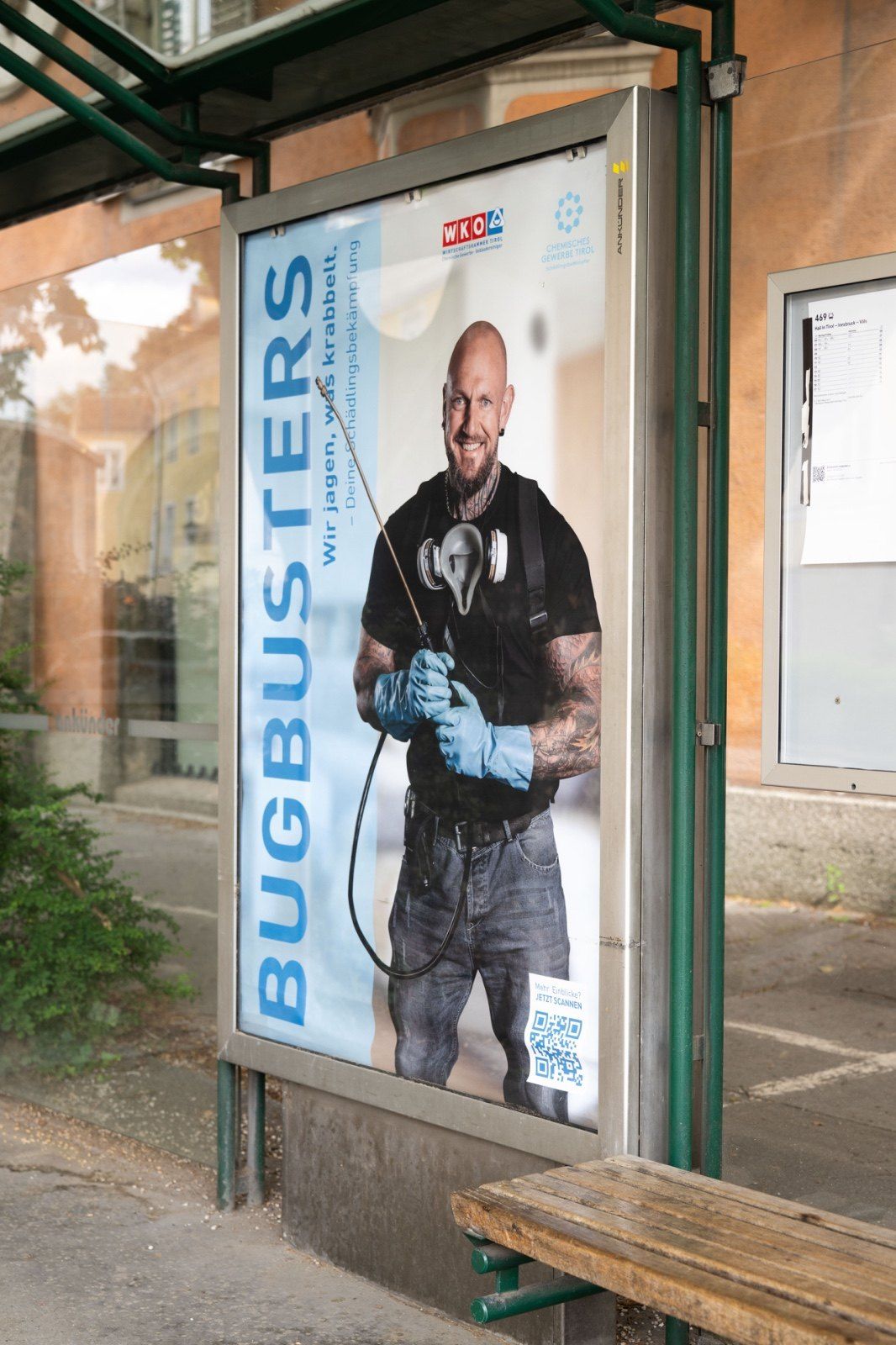 Plakat „Bugbusters – Wir jagen, was krabbelt.“ in einem Wartehäuschen: Mann mit Schutzhandschuhen und Sprühgerät